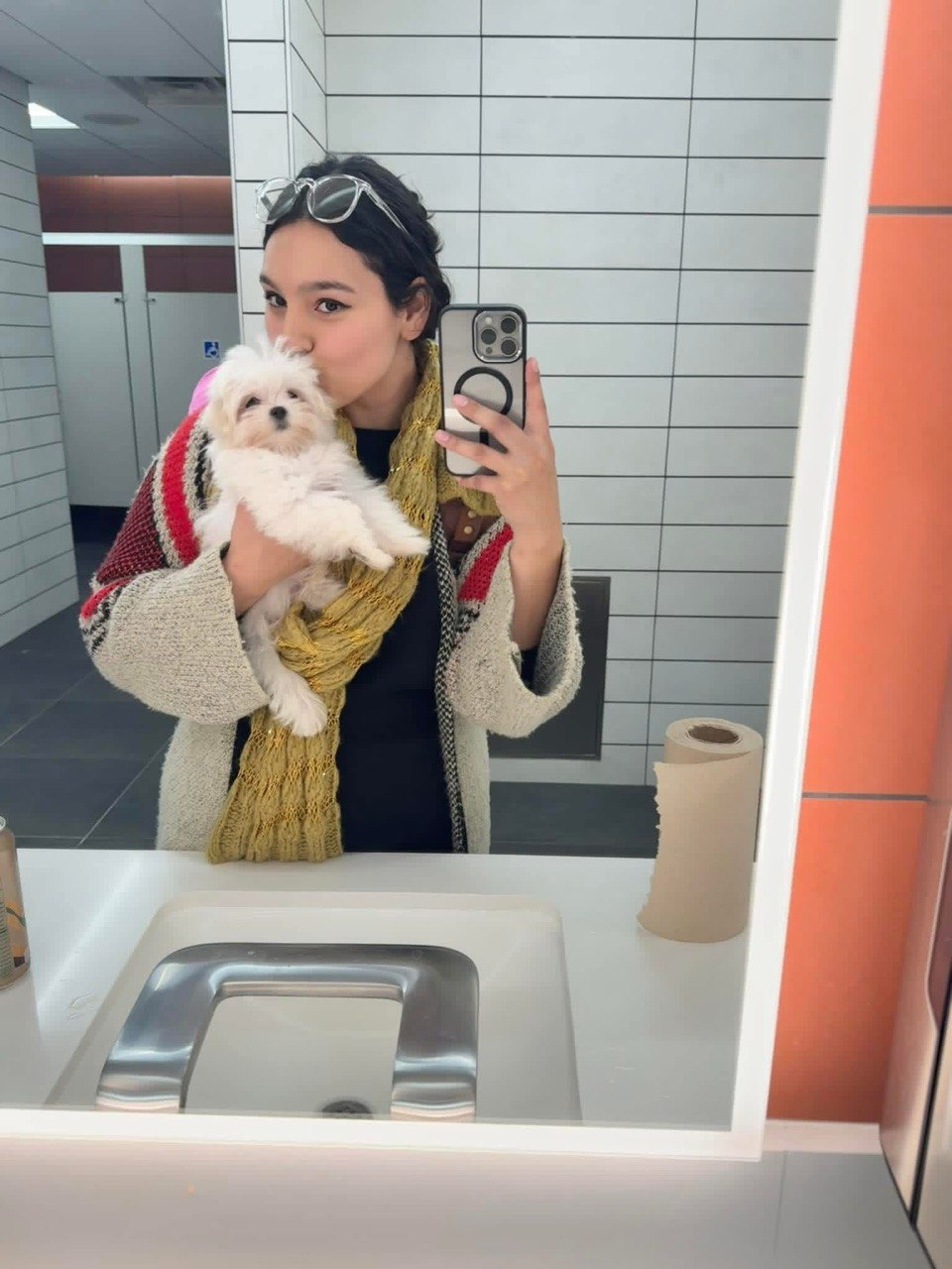 Young woman in a knitted cardigan holding a fluffy white Maltese puppy close to her face on homecoming day