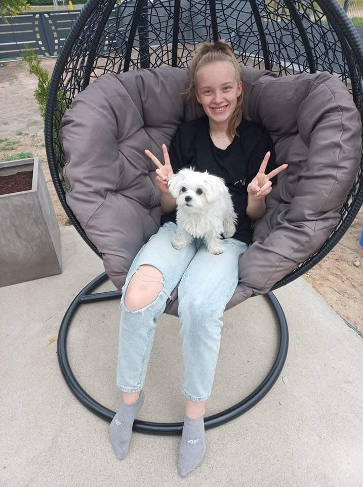 Girl sitting in a hanging garden chair with a white Maltese puppy resting on her lap