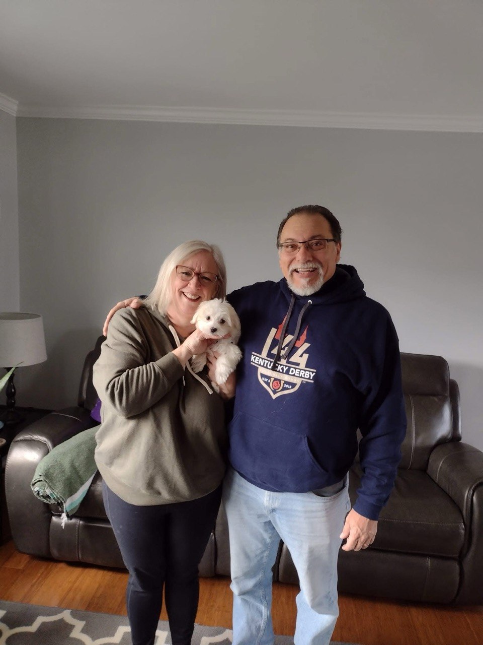 Couple holding a small white Maltese puppy together in their living room during a Pearlbrook homecoming