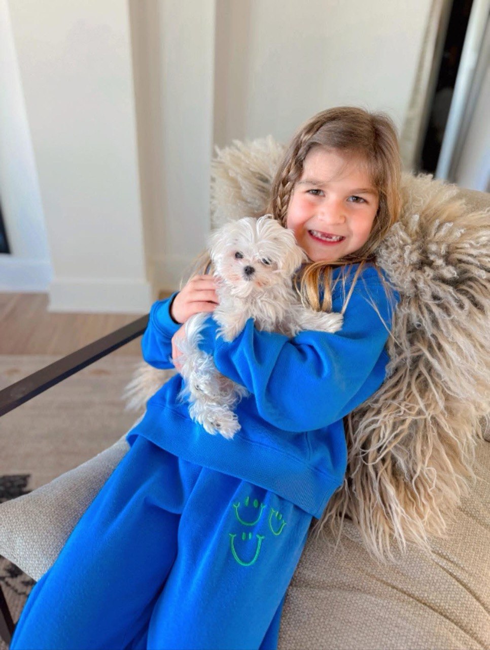 Young child smiling while gently holding a small white Maltese puppy at home